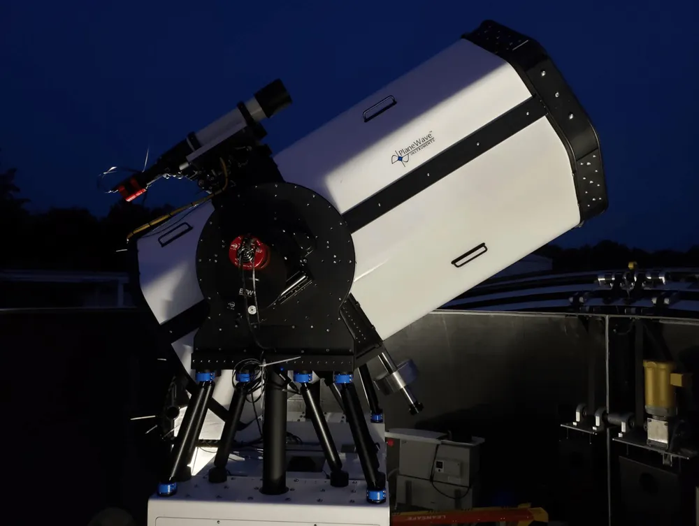 The large white telescope and tracking mount of NASA’s Low-Cost Optical Terminal under a dark blue sky.